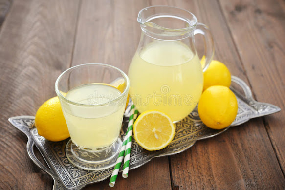 Lemon juice in a glass jar and a glass and some lemons in a tray