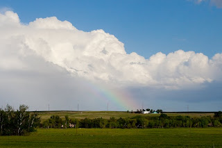 A rainbow peaks out below billowing clouds