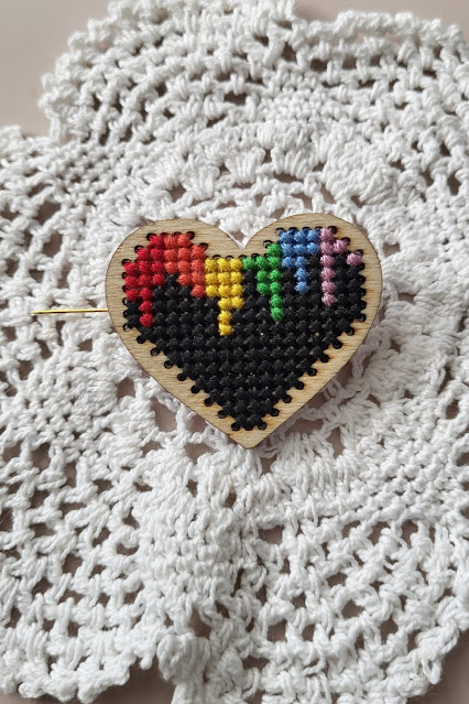 cross stitched wooden brooch with a dripping rainbow flag onto a black background