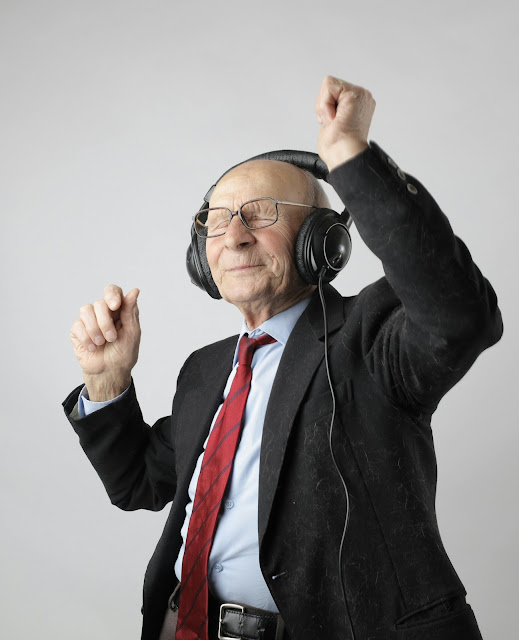 an elderly man is smiling, dancing with headphones on and his eyes closed