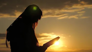 Mujer leyendo la Biblia en un atardecer con la puesta del sol