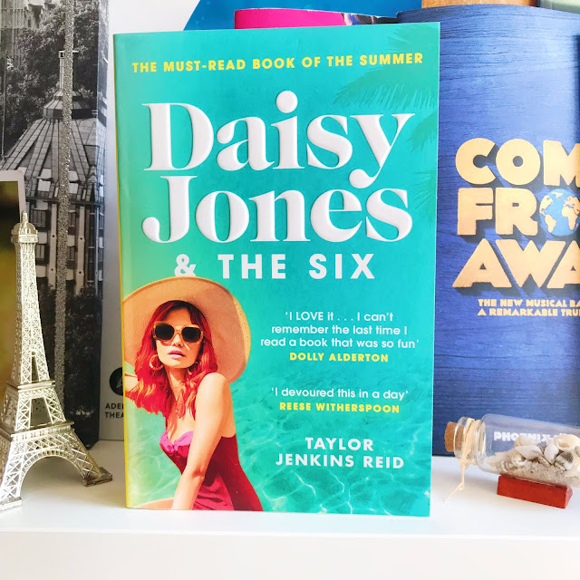 Daisy Jones & The Six by Taylor Jenkins Reid on desk shelf in front of musical programs. Ornament of Eiffel Tower next to it