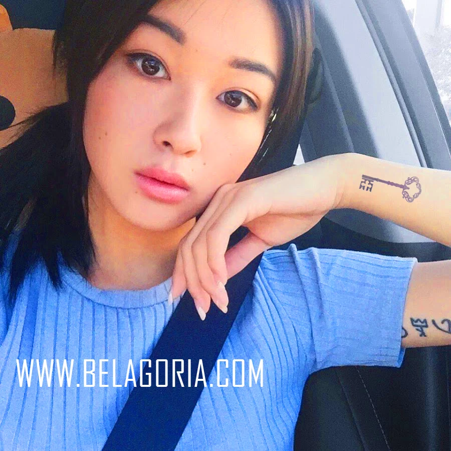 una mujer china en su coche haciendose un selfie, lleva tatuaje de llave en la muñeca