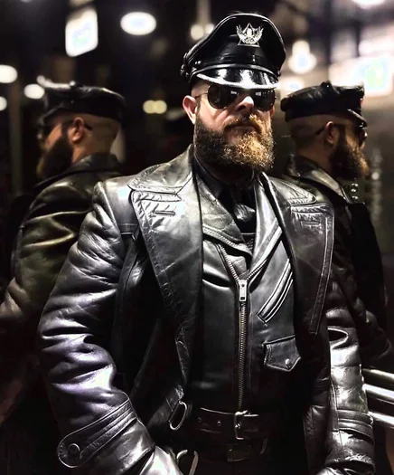 Handsome bearded stud in a uniform hat wearing a leather trench coat all black pretty badass