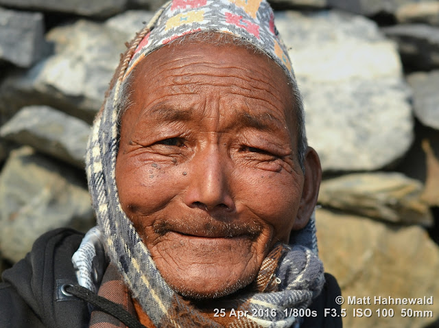 bokeh; depth of field; Syang Village; Mustang District; dhaka topi; Nepali hat; Matt Hahnewald Photography; Facing the World; photo; image; closeup; street portrait; headshot; outdoor; world cultures; cultural; one person; character; people; male; adult; ethnic; horizontal format; human; face; eyes; eye contact; photography; consent; empathy; rapport; portrait; portraiture; environmental portrait; ethnic portrait; travel portrait; travel destination; colour; 4 : 3 aspect ratio; posing; Asia; South Asia; Nepal; Himalayas; Annapurna Circuit; Nikon D3100; Nikkor AF-S 50mm f/1.8G; trekking; en face; front view; old Thakali man; wrinkles; incredible; smiling