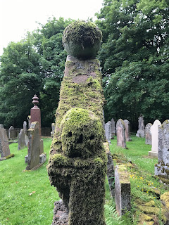 A photo of a moss covered carved skull on the side of a gravestone.  It looks vaguely comical in the way the moss has given it a soft, fluffy look.  Photograph taken by Kevin Nosferatu for the Skulferatu Project.