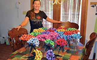 A photograph of Haley McAndrews from 2013, showing her in front of a table of over 300 colorful paper flowers that she made. Her shirt says "I heart vampires".