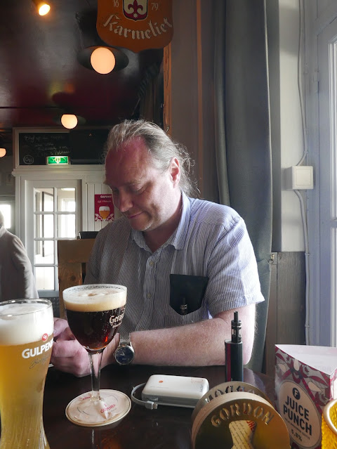 A white man in a Nederlands bar. There is a goblet-shaped glass of very dark beer in front of him.