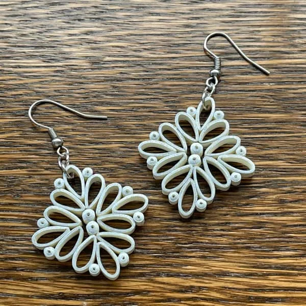 pair of square ivory paper quilled earrings with silver ear wires displayed on wooden table