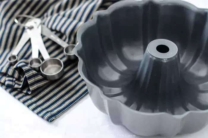 Bundt pan sitting on blue striped towel with measuring spoons.