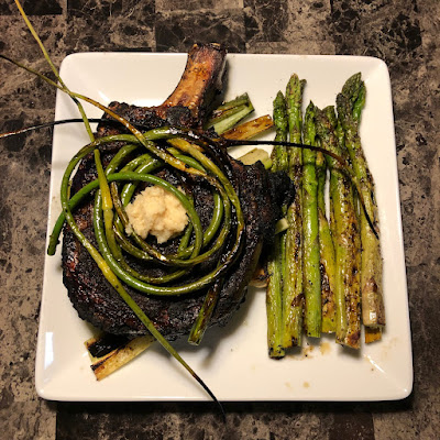 Bone-in ribeye grilled Pittsburgh rare served with some grilled asparagus and some grilled garlic scapes