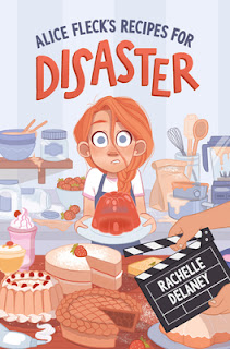Nervous looking red haired girl facing a counter with two cakes and a movie "action' sign bearing the author's namer