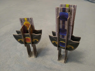 Two of the hilts, each with some tiles placed onto it. The one on the left has only three tiles, so two are connecting the crossguard pieces and only one is above the actual crossguard. The one on the right, however, has eight total tiles, so two above each crossguard, and two on each of the other two sides. On this one, all three of the tiles (both the two normal tiles and the crossguard) facing the camera have blue gems on them.