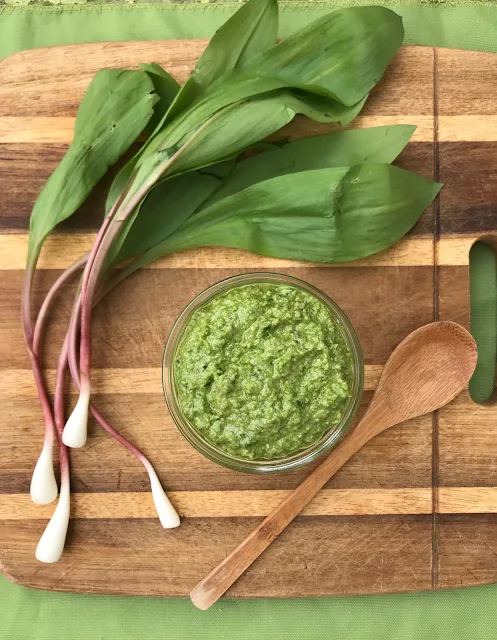 A finished jar of ramp greens pesto on a cutting board with whole ramps.