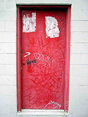 a red door with graffiti on it near a frame store in Pasadena