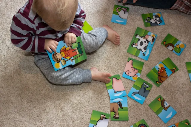 A toddler with 2 rectangles with the top and bottom of a farmer on in his lap trying to line them up