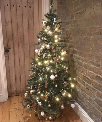 Beautiful Christmas tree in shades of white, silver and gold on a wooden floor by a stone wall and wooden door