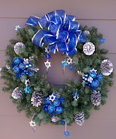 A Hannukahevergreen wreath. It's decorated with Star of David ornaments, a blue and silver bow, silver pinecones and blue sparkly ornament.