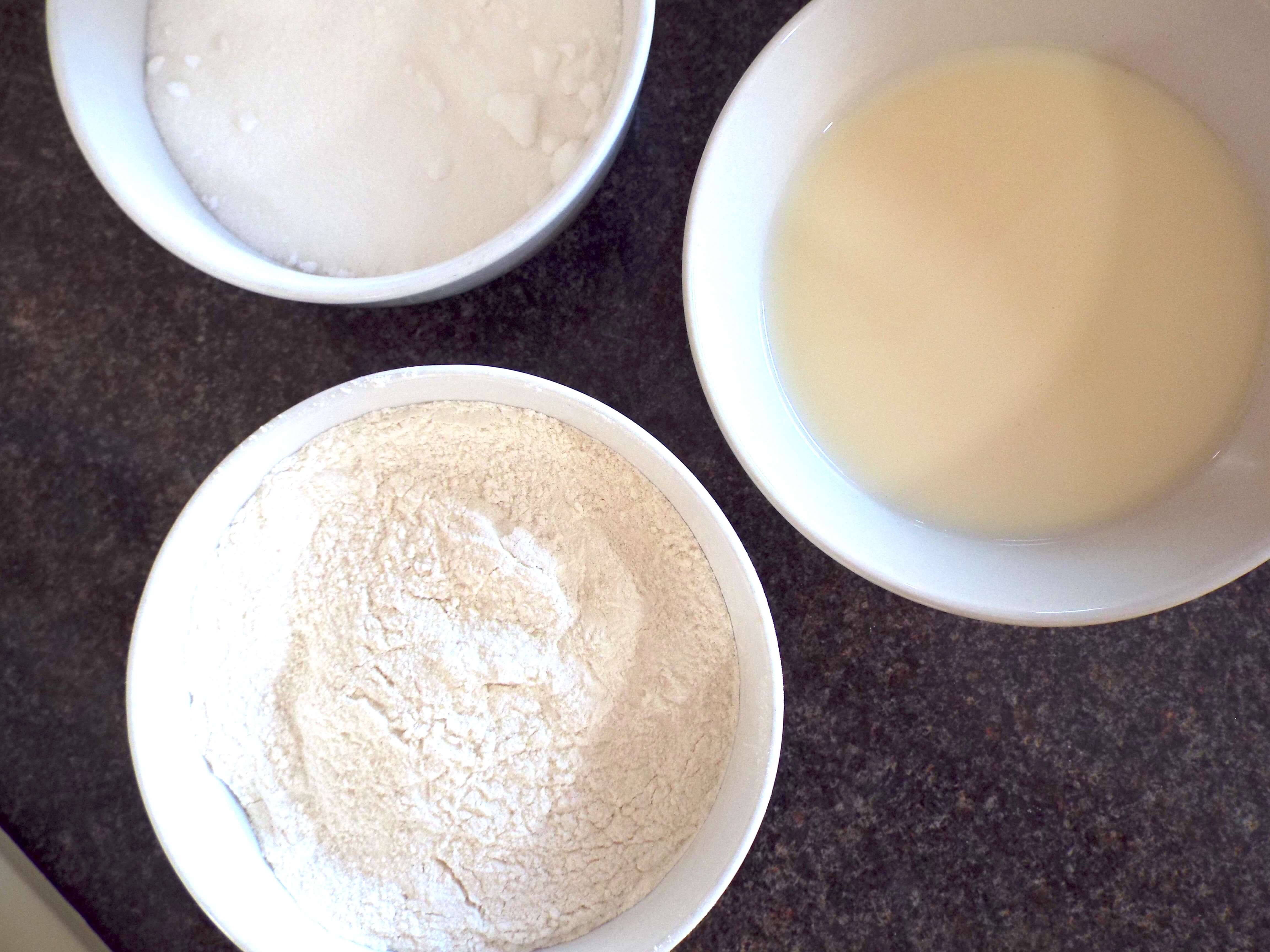 Three bowls of milk, caster sugar and flour on kitchen worktop.