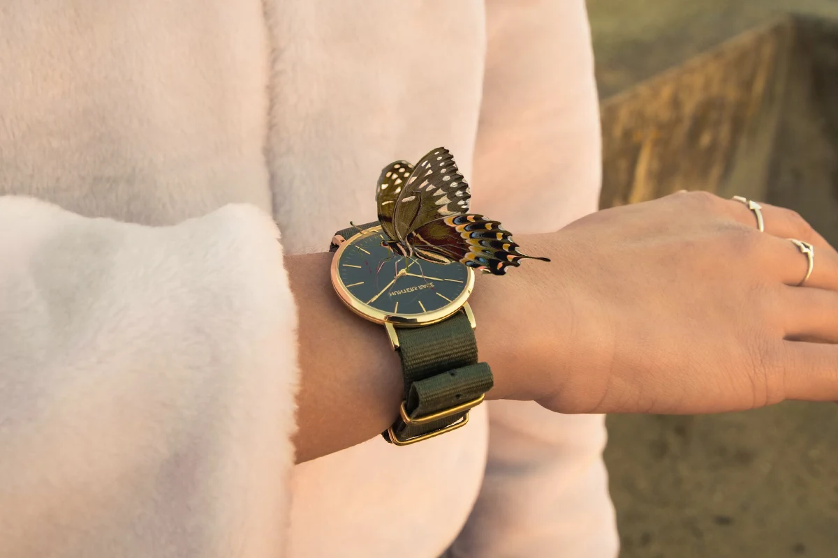 woman's hand with watch on the wrist and a butterfly sitting on top of a watch
