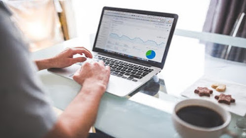 A marketer working on a computer with a smartphone, some cookies and a cup of coffee on the table.