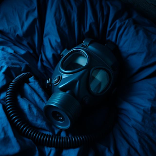 En gasmaske ligger på et blåt lagen i en seng, indikerende at blogindlægget handler om parafilier.