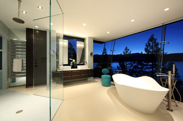 Picture of the bathroom with angled glass wall, white bathtub ans large shower cabin