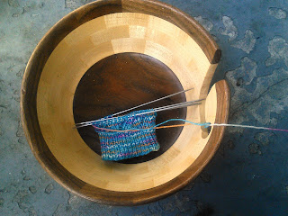 A pair of socks on double-pointed needles.  The yarn is blue flecked with yellow, white, and pink.