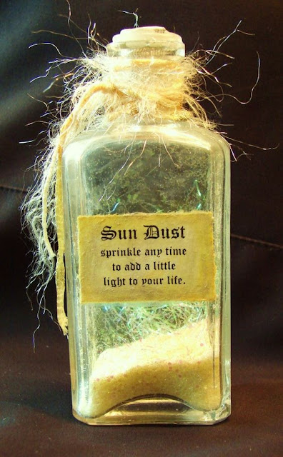 A close up of a glass bottle with a small amount of yellow powder in it, with a label printed on it saying Sun Dust sprinkle any time to add a little light to your life. The bottle has a stopper in it and is tied with string.