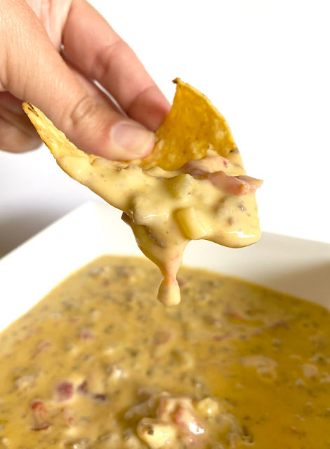 Smokey Beef Queso with leftover chili - a hand holding a tortilla chip coated in queso.