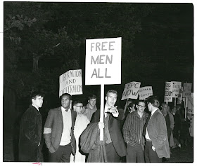 Image of dartmouth students protesting George Wallace's speech outside of Webster Hall. A student in the foreground holds a sign that reads "Free Men All."