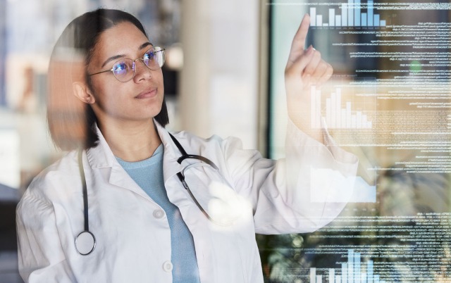 Healthcare professional with stethoscope looking at graphs and data on a screen