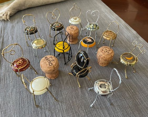 A selection of corks from bottles that have had their wire manipulated so they are turned into miniture chairs. Red, gold, white, black and crested tops make the seats look decorative. Created by Nancy Wallace.