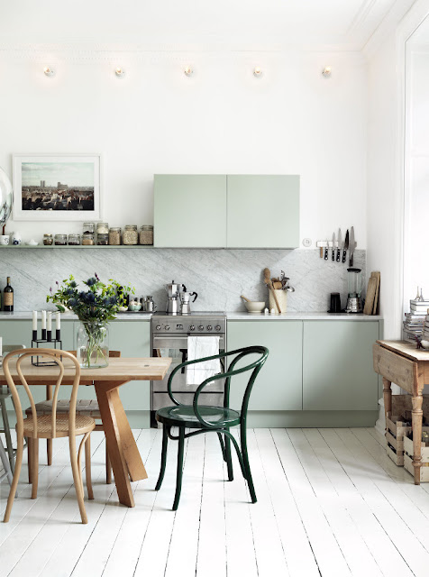 kitchen with mint green cabinets, marble slab backsplash, light wood floors, wooden table surrounded by mismatched light wood and green chairs