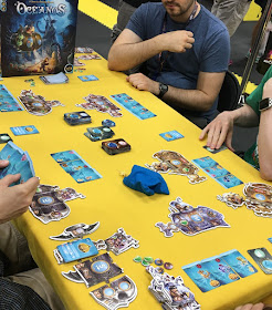 A game of Oceanos in progress at Gen Con. Four people sitting around a table with their first row of ocean cards in front of them, and their modular submarine tiles nearby.