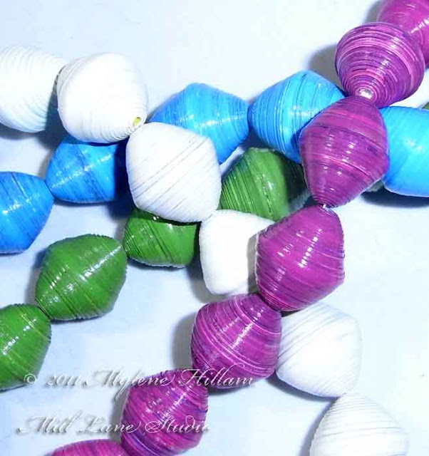 Strands of handmade paper beads in fuchsia, bright green, turquoise and white.