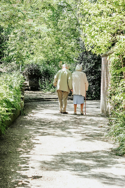 elderly couple walking down tree lined path:Photo by micheile henderson on Unsplash