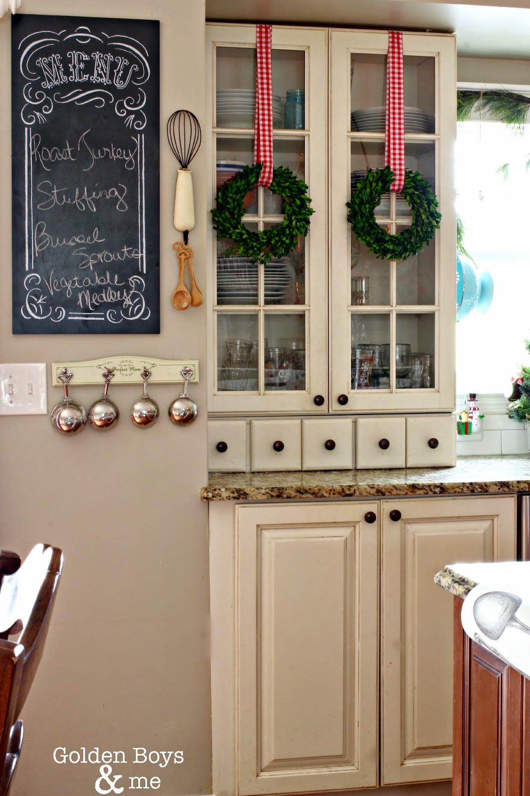 Preserved boxwood wreaths hung on glass cabinet doors in Christmas kitchen.-www.goldenboysandme.com