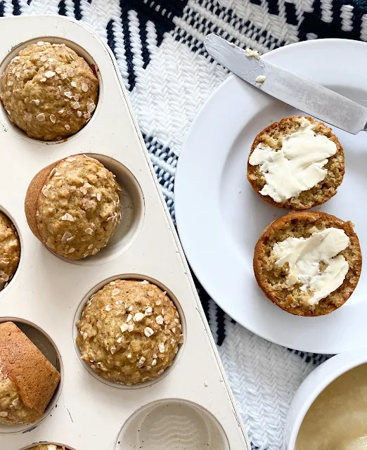 Applesauce oatmeal muffins in a muffin tray and served on a white plate with butter.