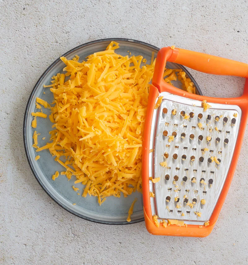 Grated cheese on a blue plate with an orange grater.