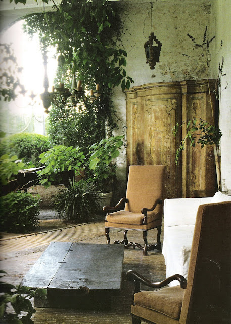 Outdoor living with vine-covered walls, foliage, upholstered chairs, chandelier, hanging lanterns, antique cabinet and white slipcover, image from Timless Interiors by Axel Vervoordt, edited by lb for linenandlavender.net (l&l)