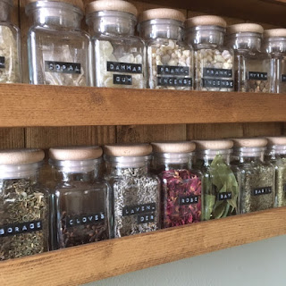 Wooden wall-mounted apothecary jar holder containing multiple jars with herbs in