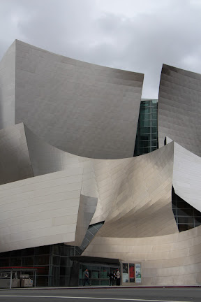 Walt Disney Concert Hall, seen from across the street. Masses of stainless steel rising into the air and a broad band of the same across the street-level facade.