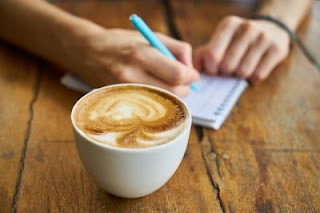 hands of person who is trying to find their writing style with pen and note on a table with cup of coffe