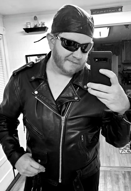 BW bear biker from waist up wearing black leather bandana, biker jacket & dark shades taking selfie
