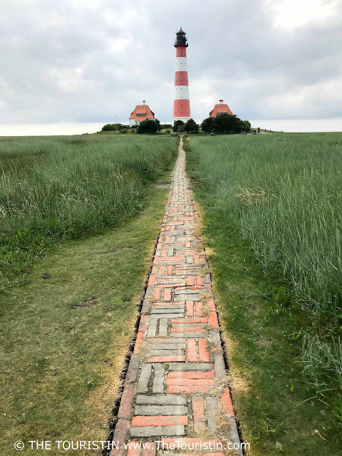 A long and narrow red brick path leading to a red and white lighthouse