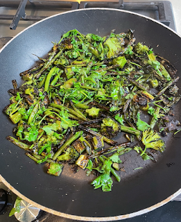 A large frying pan is on a gas hob. It has green veg (broccoli, green beans, and coriander) with all the edges blackened and charred.