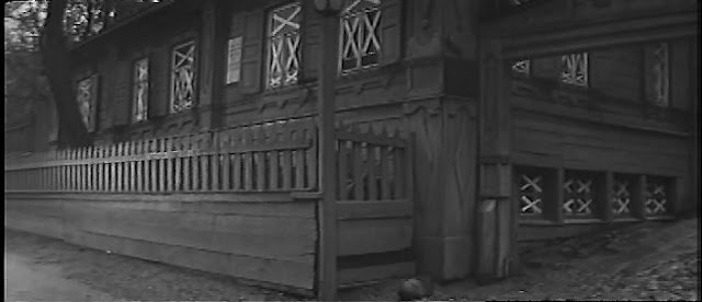 Черно-белый кадр фильма с изображением дома с заборчиком
