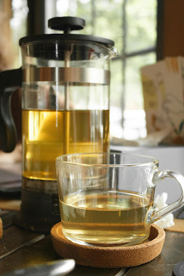 Shows green tea in glass tea pot and sitting in glass on table ready for consumption
