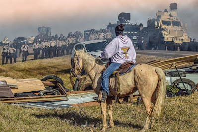 color photograph of woman on horse facing down armed police at Standing Roock protest, 2016